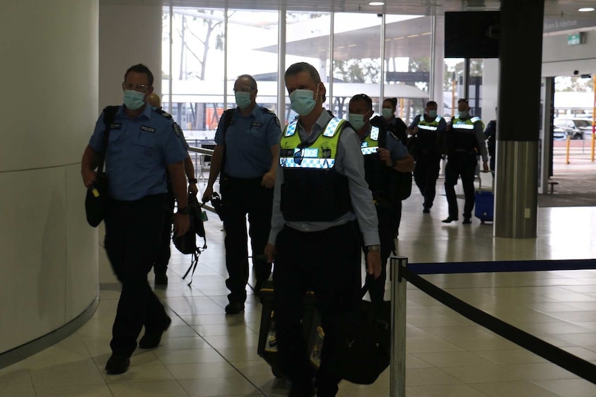 Police are seen wearing face masks as they walk through a white and grey building with a glass wall behind them.