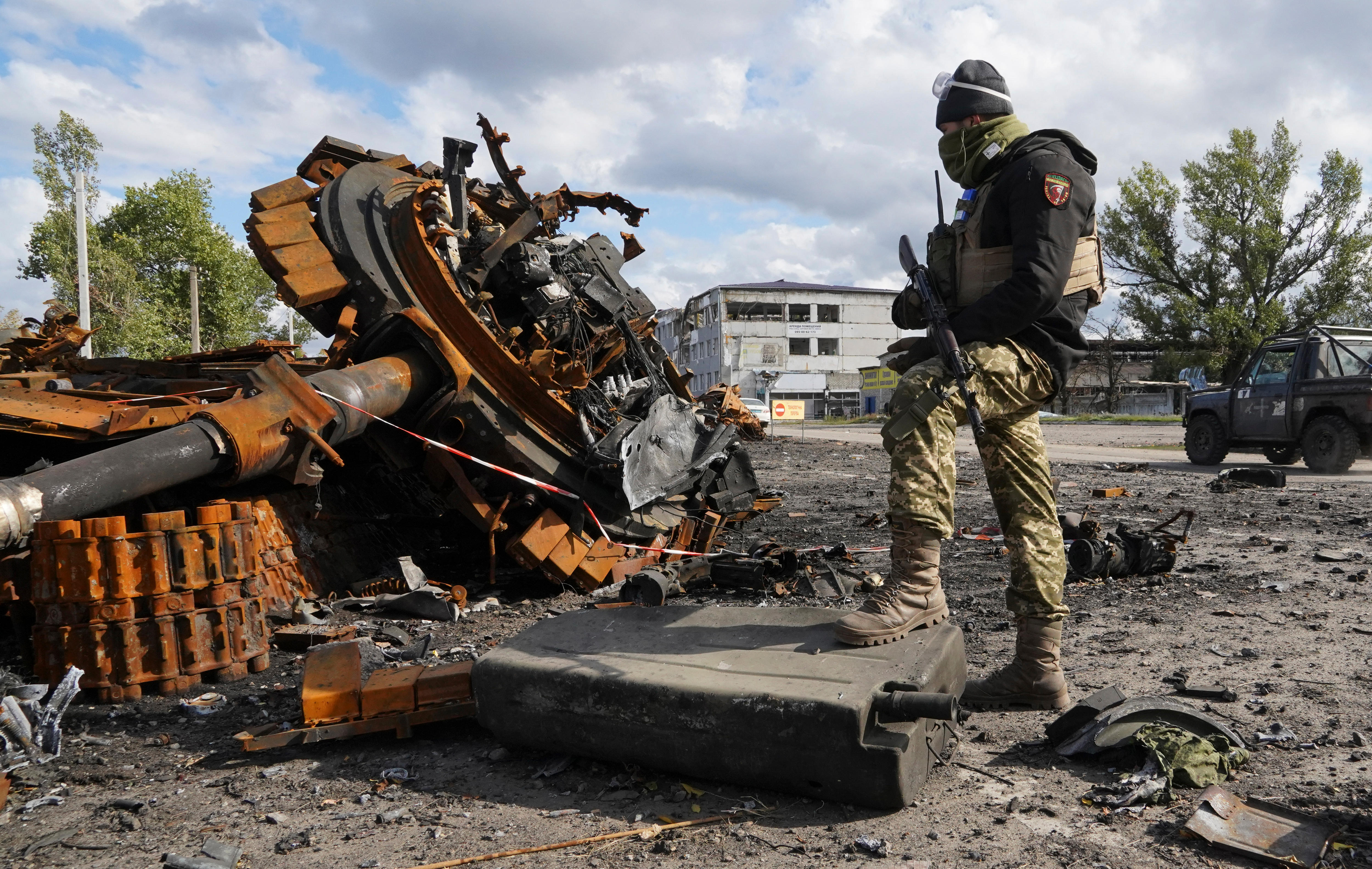 A Ukrainian soldier stands near a damaged Russian tank.