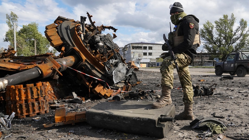 A Ukrainian soldier stands near a damaged Russian tank.