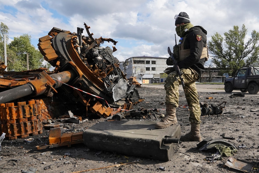 A Ukrainian soldier stands near a damaged Russian tank.