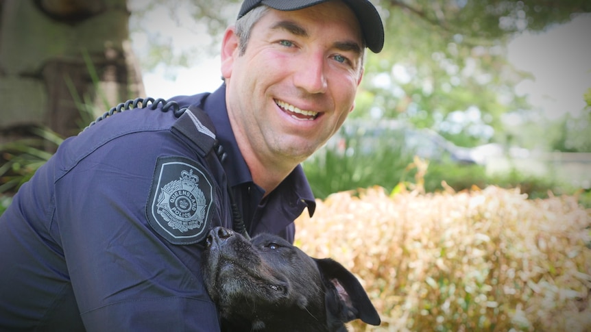 Black Labrador leaning on smiling police officer crouching down 