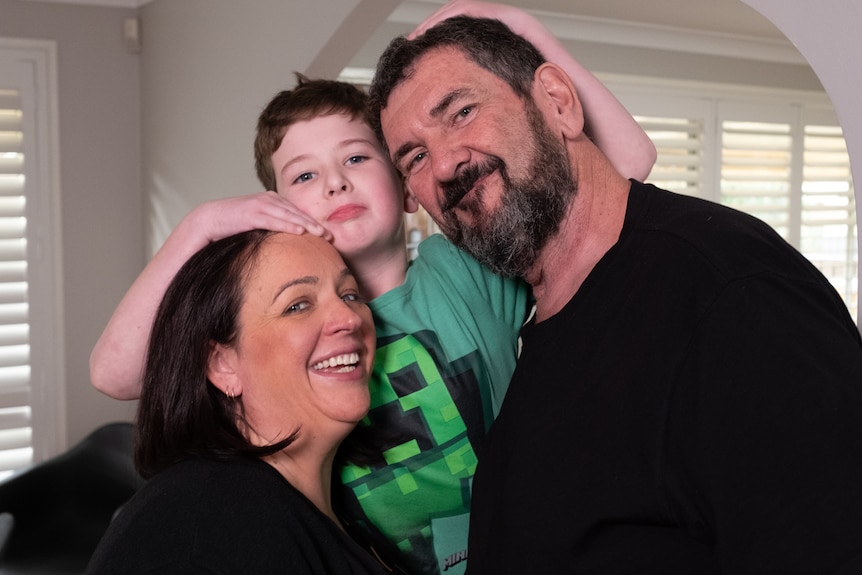 A mum, dad and son cuddle eachother, smiling at the camera