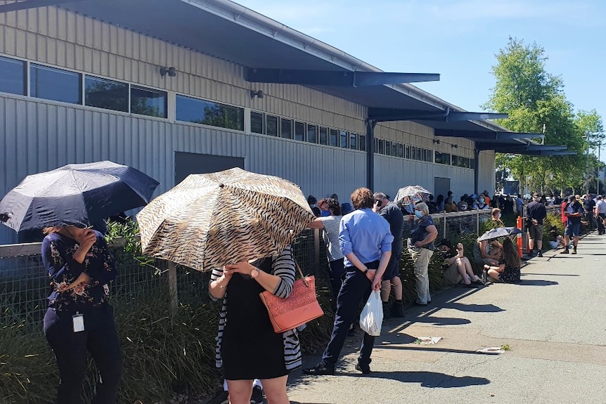 Dozens of people are seen lining up for coronavirus testing next to a building in Shepparton, some are standing under umbrellas.