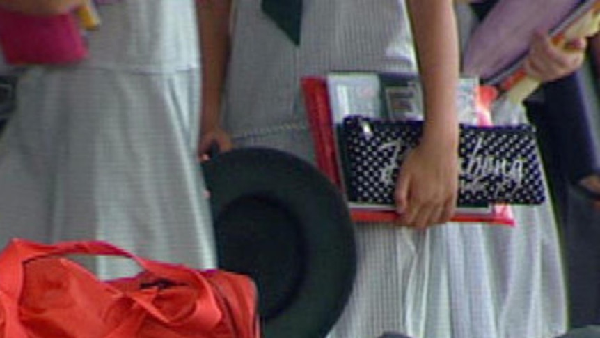 School children carry books with bags in foreground.