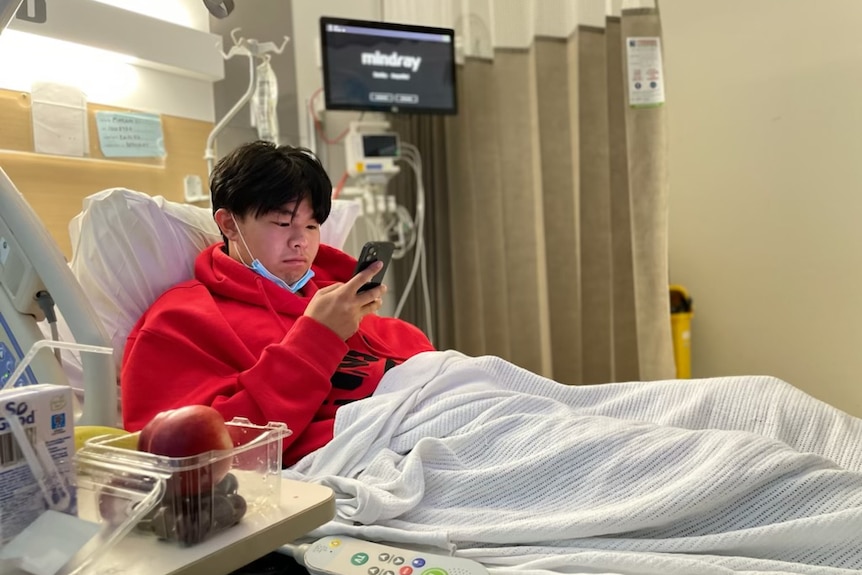Lee Li looks at his mobile phone as he sits up in a hospital bed.
