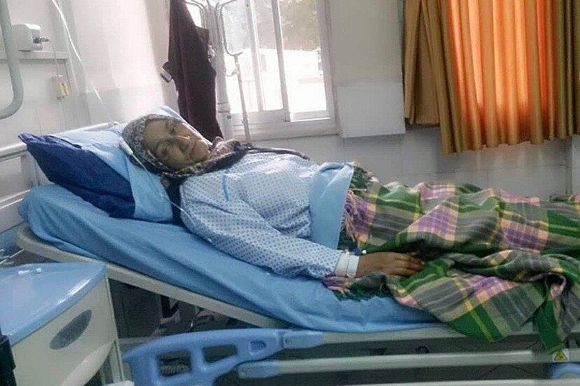 An elderly woman lying on a hospital bed.
