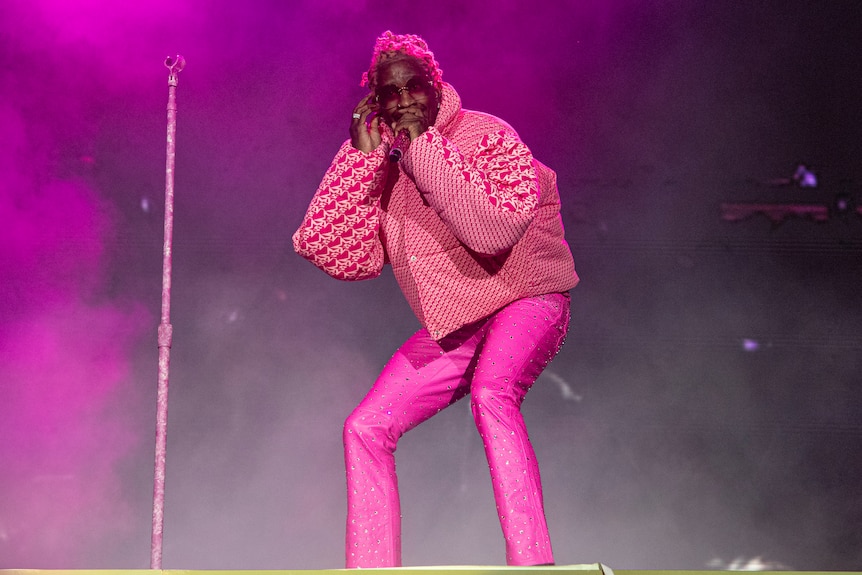 Young Thug, dressed in pink pants and a pink jacket, sings into a microphone on stage.