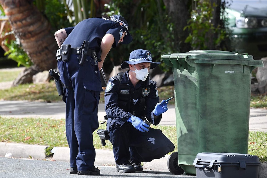 Police dust a wheelie bin for fingerprints outside a house at Deception Bay.