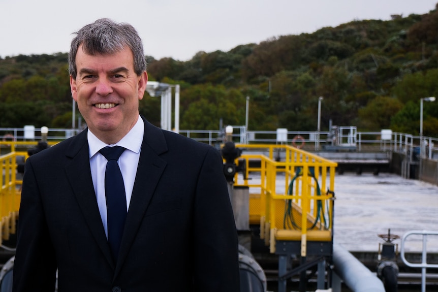 A man in a suit standing in front of a water treatment plant