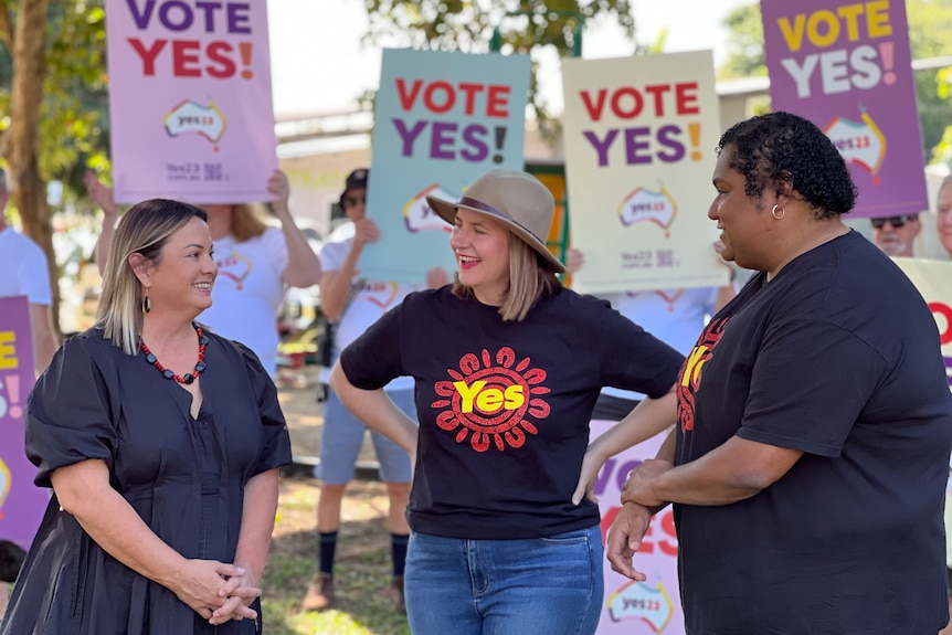 Three women standing in front of people holding 'Vote Yes' signs