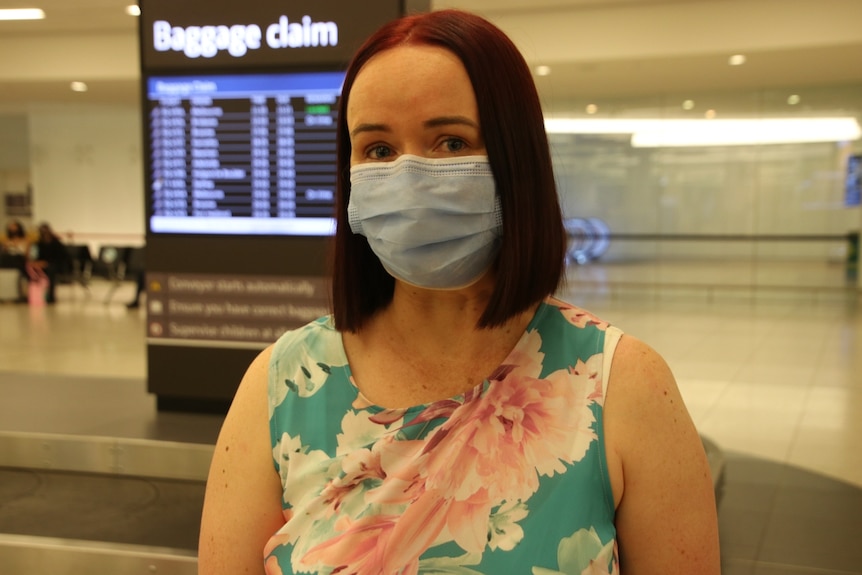 Kim Virgo in a blue mask looking at the camera while at baggage claim in an airport