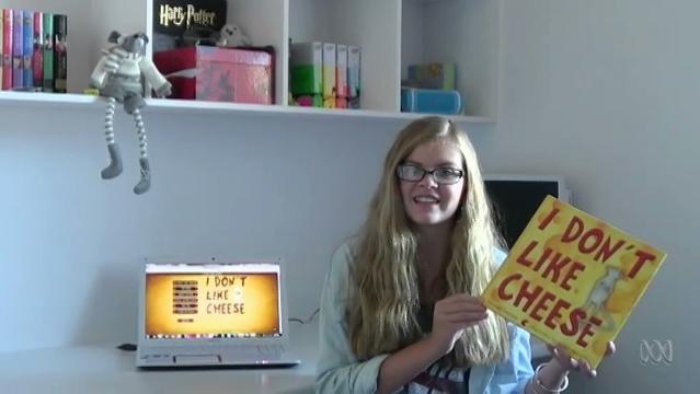 A teenage girl in a room holds a book with title that reads "I don't like cheese"