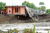 A group of people inspect a building that has collpased into a waterway after being undermined by floodwaters. 