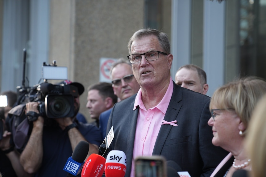 A man wearing glasses addresses the media