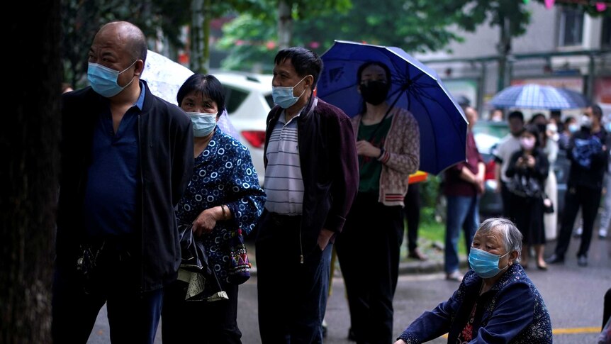 Residents wearing face masks wait in line for nucleic acid testing amid rainfall.