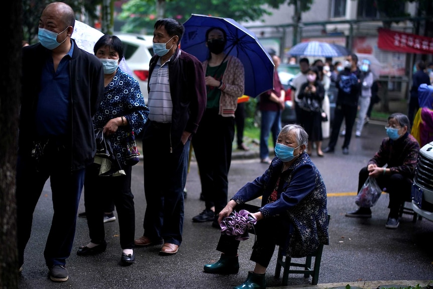 Residents wearing face masks wait in line for nucleic acid testing amid rainfall.