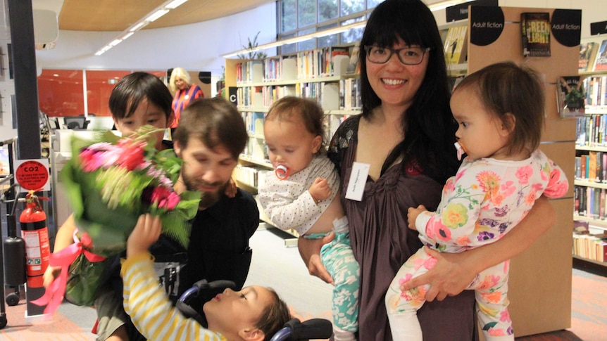 Anh Nguyen holds a twin in each arm and her partner has one of their sons on his back and the second in a wheelchair.