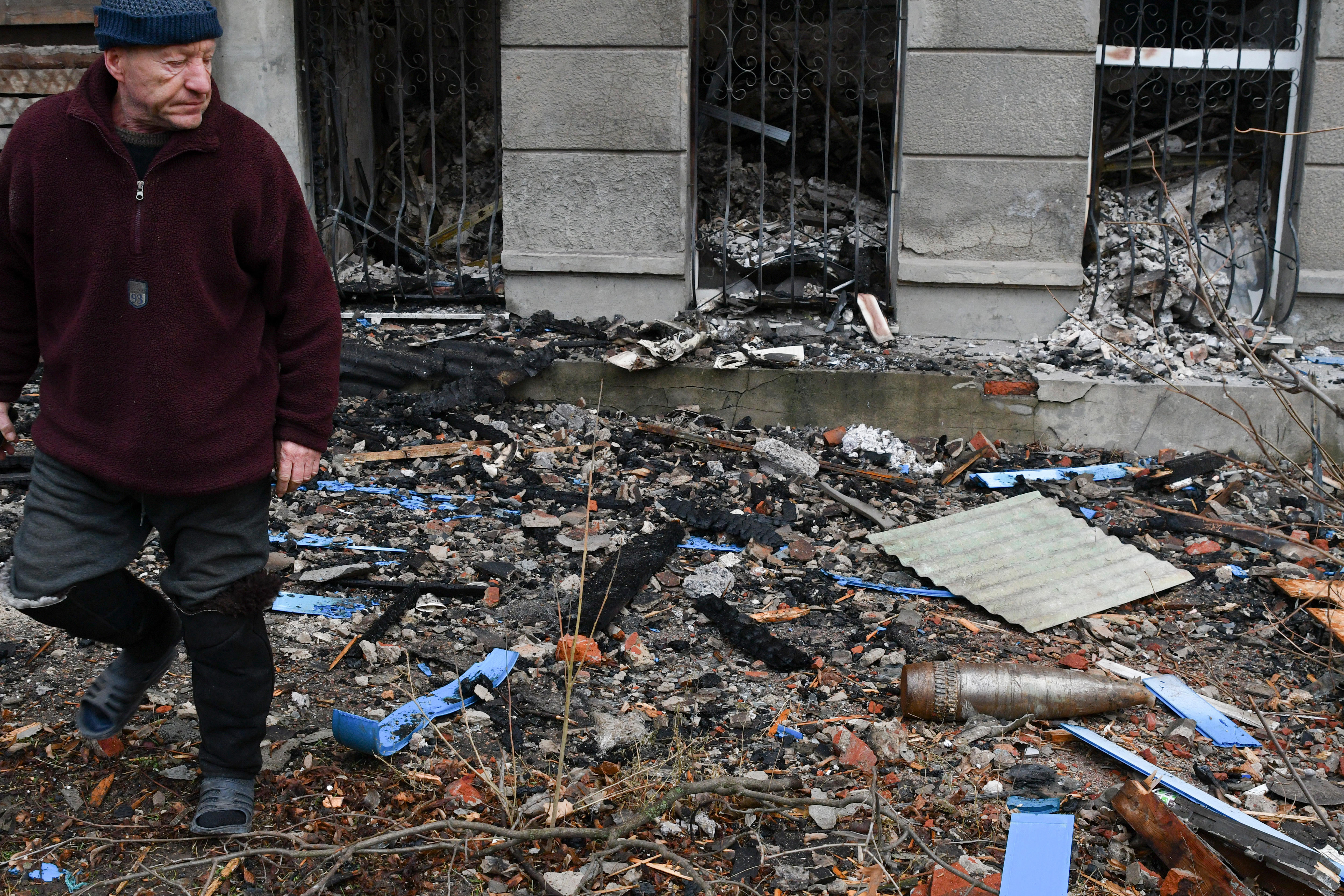 A man passes by an unexploded shell lying in debris. 