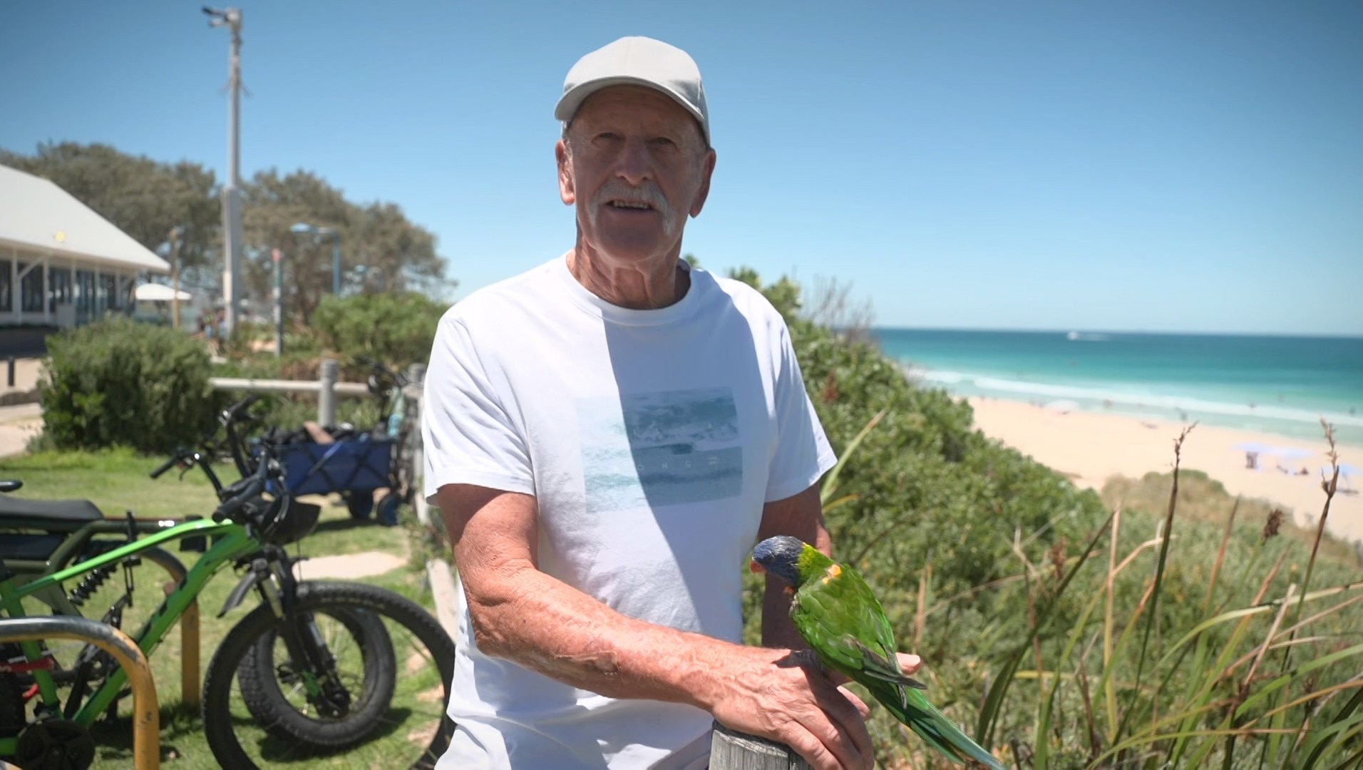 El señor Newton se sienta en la playa con su lorito arcoíris "kuta".