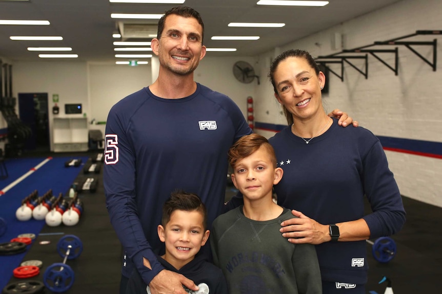 Fiona and Shain stand with their two children in their gym, with equipment behind them.