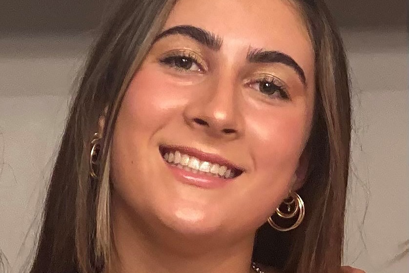 A head and shoulders shot of a smiling teenage girl with brown hair and gold necklaces on.