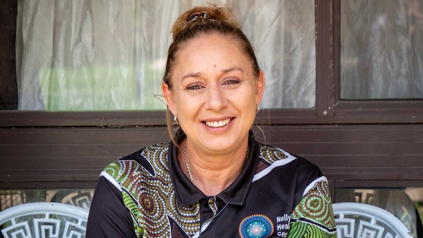 Helen Eason smiling in a polo shirt with Indigenous designs on it.