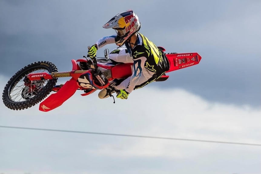 Motocross racer on red dirtbike sailing through the air after hitting a jump