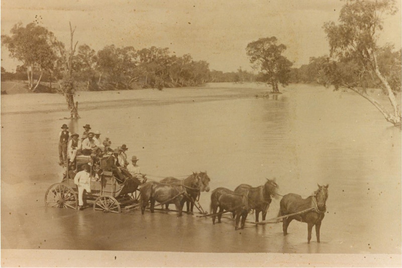 A horse drawn stagecoach stopped in a flooded river black and white