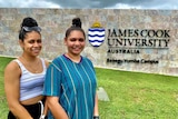 Two young Indigenous girls stands in front of a JCU sign.