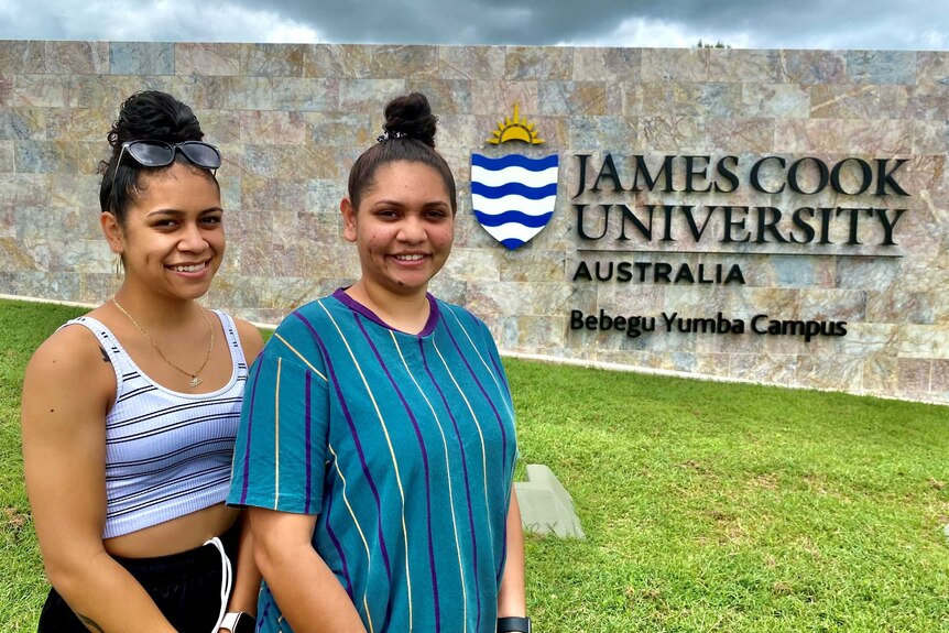 Two young Indigenous girls stands in front of a JCU sign.
