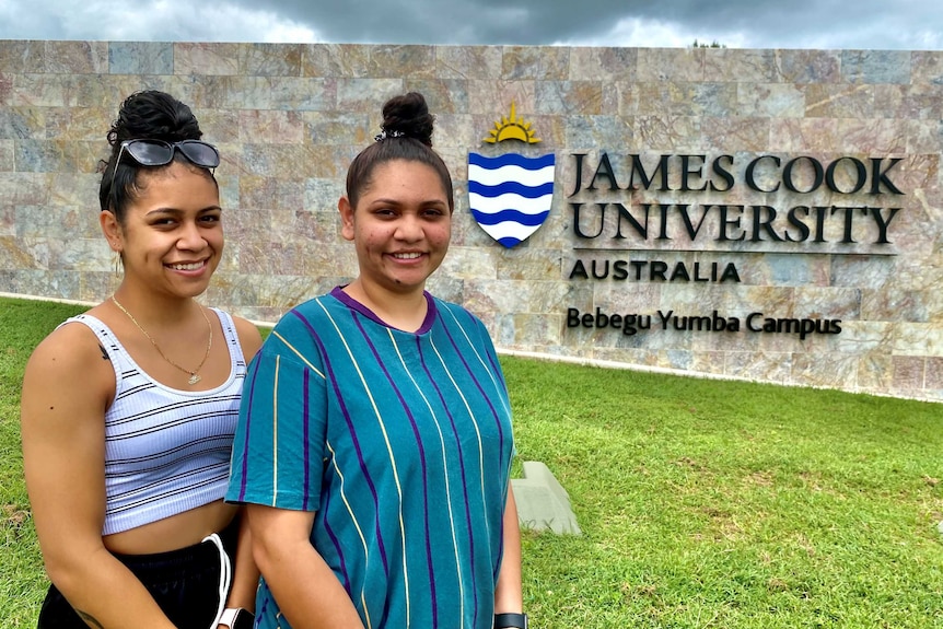 Two young Indigenous girls stands in front of a JCU sign.