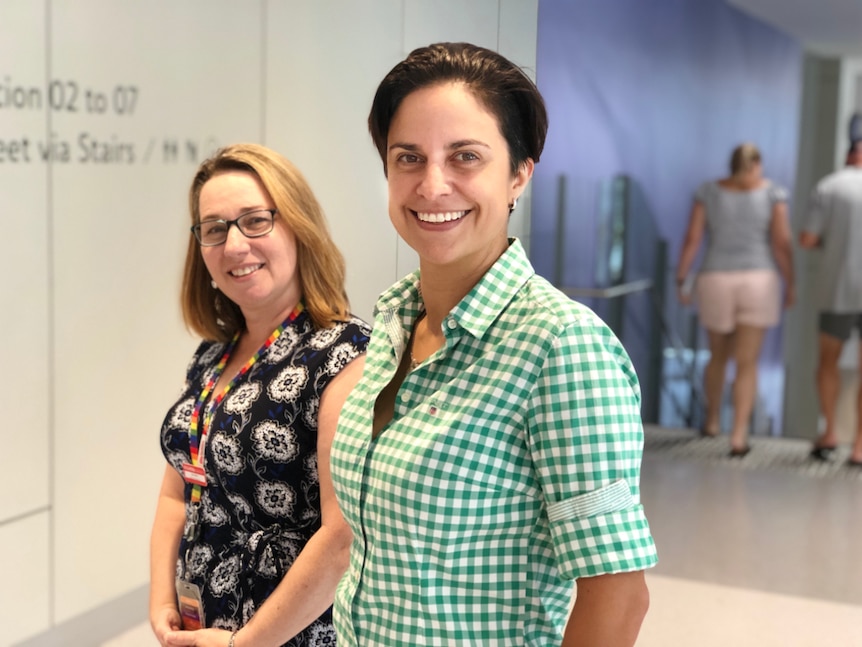 Two women who are doctors, standing in the foyer of a hospital smiling.