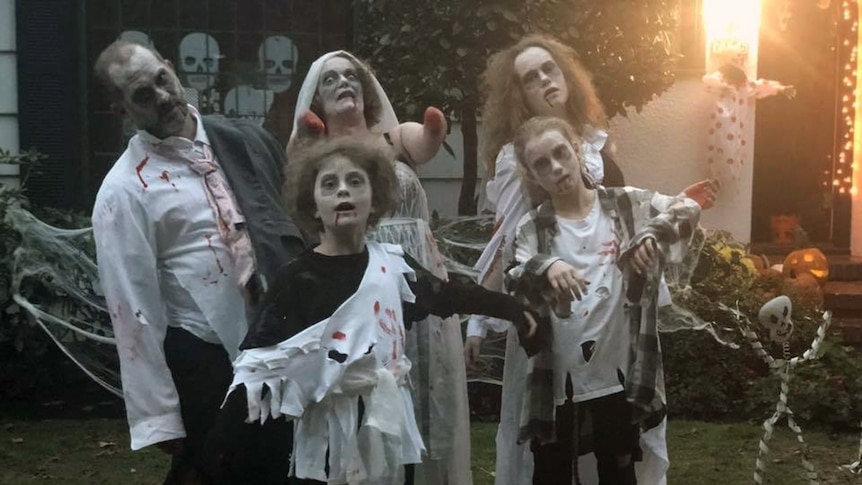 Man, woman and three children dressed up as zombies. Woman has no hands or forearms, fake blood painted on ends of her arms.