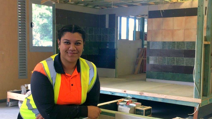 TJ Pamo, a young trainee carpenter, leans on a wall in her hi-vis uniform