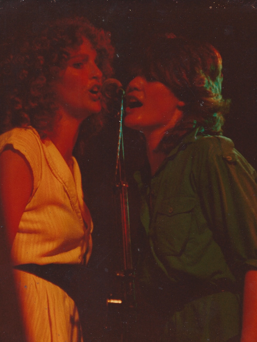Two women sing into a microphone live on stage