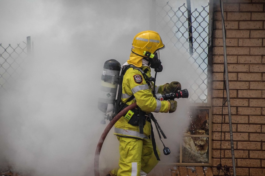 An unidentified firefighter wearing high-vis work uniform and using a hose to put out a house fire.