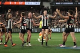 A group of Collingwood AFL players stand with arms raised in triumph after the final siren in a finals game.