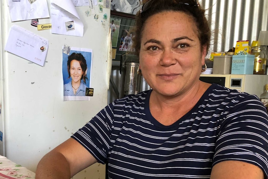 mother sitting on bench with photo of deceased daughter on a fridge behind her