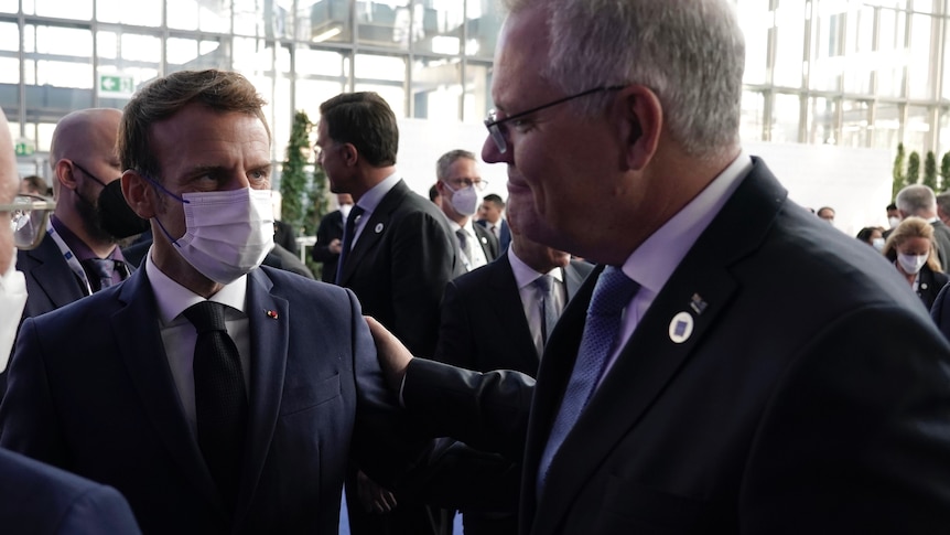 A photo of French President Macron, who's wearing a mask, and Scott Morrison with his hand on Macron's shoulder.