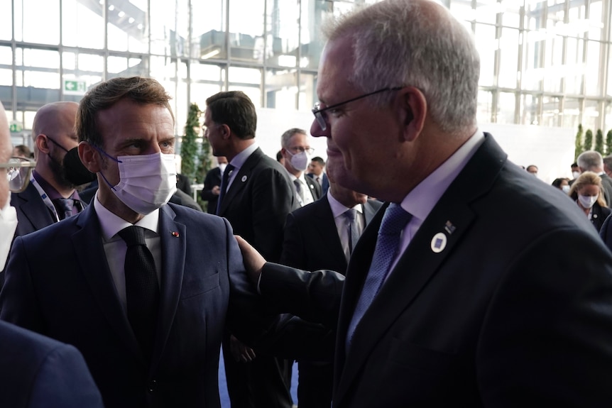 A photo of French President Macron wearing a mask and Scott Morrison with his hand on Macron's shoulder.