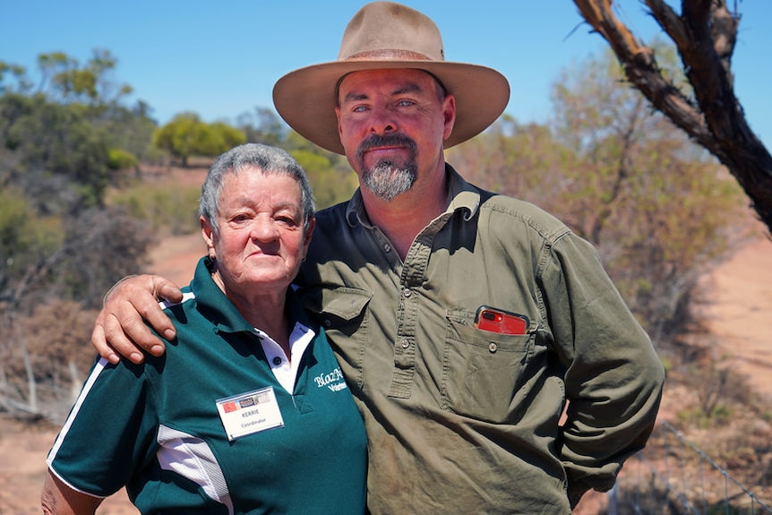 A man and woman with an arm around each other in an outback setting.