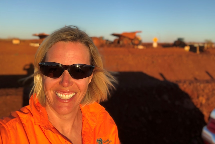 Betsy wears sunglasses and a bright orange work shirt on a mine site