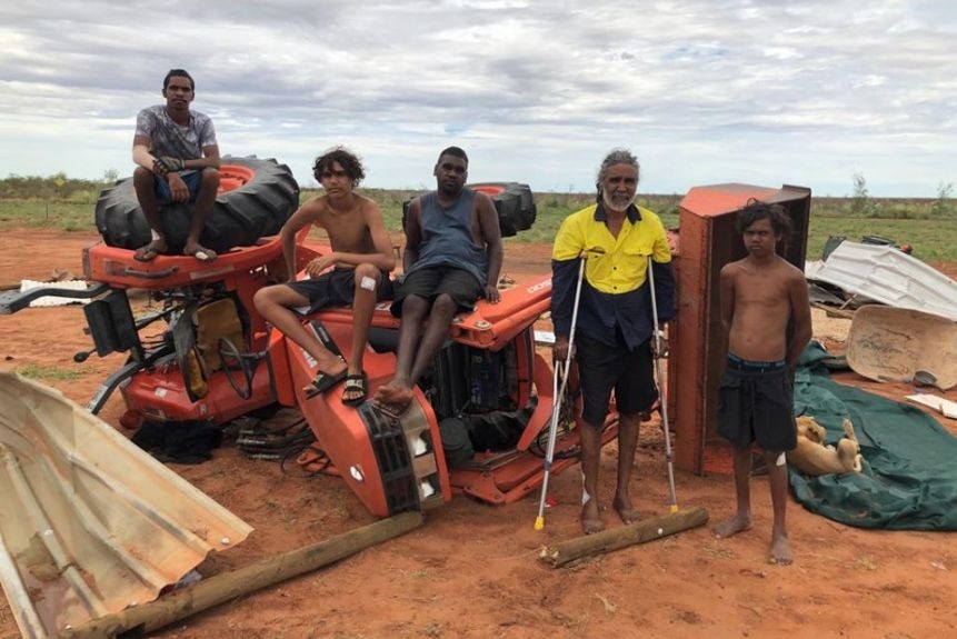 A family stands in front of flipper tractor and destroyed tin shed in remote Aboriginal community