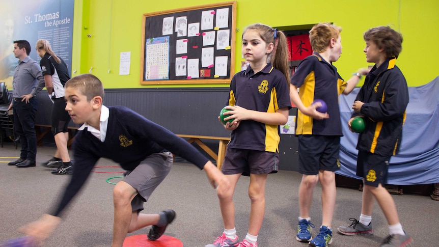 Primary school students line up to try playing lawn bowls