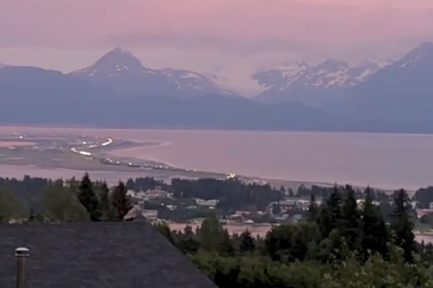 A serene dusk view of a lakeside town with snowcapped mountains behind.