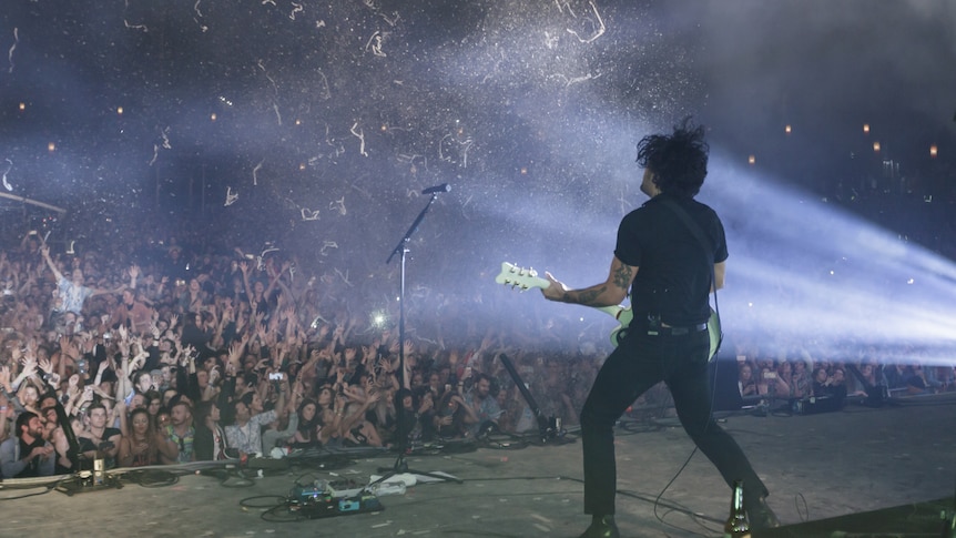 Confetti flies through the air into a massive crowd. Dave from Gang Of Youths is facing the crowd, back to camera.