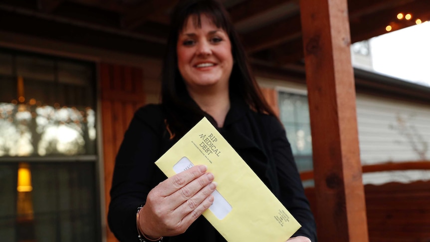 A woman holds a bright yellow envelope that confirms that her medical debt has been erased on her house's front verandah.