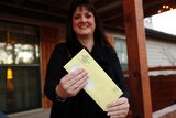 A woman holds a bright yellow envelope that confirms that her medical debt has been erased on her house's front verandah.