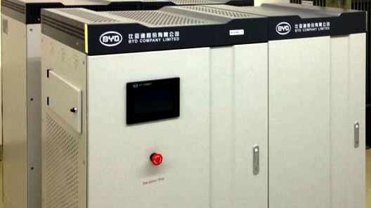 A BYD lithium battery in a tall rectangular metal case sits on the ground.