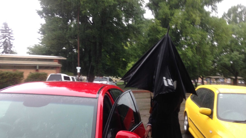 Christopher Luke Evans hiding under an umbrella as he gets into a car in Goulburn.